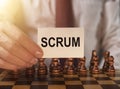 Scrum word on paper in businessman hand close up over chessboard. Concept of methods in management