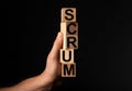 Scrum word on wood cube blocs in male hand over black background. Concept of methods in management