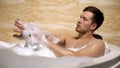 Scrupulous man soaping himself with loofah, taking bath with foam, cleanness