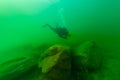 SCUBA diver exploring a cloudy inland lake and boulders with a diving torch