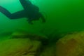 SCUBA diver exploring a cloudy inland lake and boulders with a diving torch