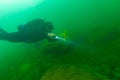 SCUBA diver exploring a cloudy inland lake and boulders with a diving torch