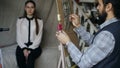 Sculptor creating sculpture of human`s face on canvas while young woman posing him in art studio