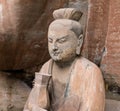 Statue of disciple or follower holding bottle in front of giant Buddha at Dazu Rock Carvings