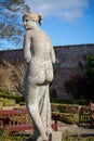 Sculpture of a figure situated in a lush green park setting, next to a wooden outdoor bench