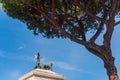 The sculpture of Goddess Victoria riding on quadriga seen through green pine. The top of Monument Vittorio Emanuele II