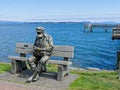 Sculpture of a man on the sitting on the bench at the shore with mask