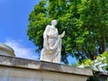 Sculpture of Roman official made of white stone with large green tree in the background