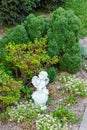 Sculpture of a small angel with a chin resting in the park near green bushes and flowers. Royalty Free Stock Photo