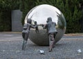 Sculpture with two life sized bronze figurines pushing a large polished stainles steel ball in Dallas, Texas.