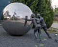 Sculpture with two life sized bronze figurines pushing a large polished stainles steel ball in Dallas, Texas.