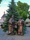 Sculpture of two saints standing near the elegant green fir tree on the background of a small chapel and the golden