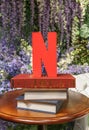 Scupture of a red letter N, initial and symbol mark of Netflix on a stack of books on a table.