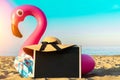 Sea background. Funny pink toy flamingo with blackboard, slippers and hat for text on summer ocean nature beach background in Royalty Free Stock Photo