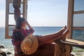 Sea background. Outdoors lifestyle fashion portrait stunning girl sitting back on the beach. Wearing stylish blue dress, straw