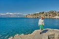 Sea bay near old city in Turkish Antalya and lonely young woman on ruins of old pier in early spring on sunny day.