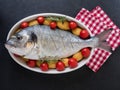 Sea bream, tomatos, potatos and rosemary on a serving dish on slate background. ready to cook