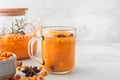 Sea buckthorn autumn tea with orange in glass cup and teapot with fresh berries, cinnamon and rosemary on white table