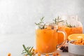 Sea buckthorn autumn tea with orange in glass cups with fresh berries, cinnamon and rosemary on white table