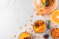 Sea buckthorn autumn tea with orange in glass cups with fresh berries, cinnamon and rosemary on white table. Top view