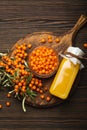 Sea buckthorn healthy drink in bottle, ripe berries in glass jar and branches with leaves top view on dark wooden rustic Royalty Free Stock Photo