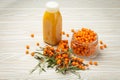 Sea buckthorn healthy drink in bottle, ripe berries in glass jar and branches with leaves top view on white wooden Royalty Free Stock Photo