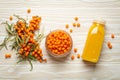 Sea buckthorn healthy drink in bottle, ripe berries in glass jar and branches with leaves top view on white wooden Royalty Free Stock Photo