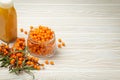 Sea buckthorn healthy drink in bottle, ripe berries in glass jar and branches with leaves top view on white wooden Royalty Free Stock Photo