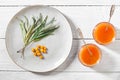 Sea buckthorn jam and fresh berries in glass jars and a green branch on a plate