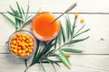 Sea buckthorn jam and fresh berries in glass jars and a green branch on a white wooden table Royalty Free Stock Photo