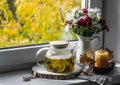 Sea buckthorn tea with herbs in a glass teapot on the window. Cozy home autumn still life