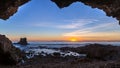 Sea cave at sunset with light clouds and pink and orange hues over the Pacific Ocean in Orange County, California.