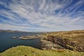 Sea cliff with low headland in the background and blue sky with white cirrus clouds