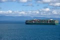 Large, green, cargo container ship sailing near sea coast.