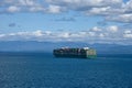 Large, green, cargo container ship sailing near sea coast.