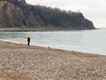 A sea coastal strip of land, cloudy weather, a lonely figure of a woman walking along the seashore on a summer day.