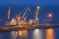 Sea commercial port at night in Mariupol, Ukraine. Industrial view. Cargo freight ship with working cranes bridge in sea port