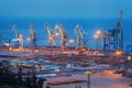 Sea commercial port at night in Mariupol, Ukraine. Industrial view. Cargo freight ship with working cranes bridge in sea port