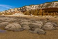 Sea eroded boulders protrude from the sand in front of the white, red and orange stratified chalk cliffs at Old Hunstanton