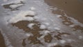 Sea foam being blown by the wind on sandy beach in slow motion. Spume flow pieces on a shore by the ocean waves on windy