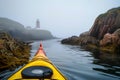 sea kayak by rocky cove, lighthouse in distance, mist Royalty Free Stock Photo