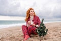 Sea Lady in plaid shirt with a mug in her hands enjoys beach with Christmas tree. Coastal area. Christmas, New Year