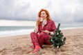 Sea Lady in plaid shirt with a mug in her hands enjoys beach with Christmas tree. Coastal area. Christmas, New Year