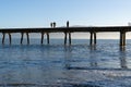 From sea level silhouettes of people on long historic Tokomaru Bay Wharf projecting into bay