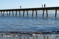 From sea level silhouettes of people on long historic Tokomaru Bay Wharf projecting into bay