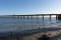 From sea level silhouettes of small figures of three people walking along long historic Wharf projecting into bay