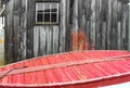 By the sea - Old weathered building behind the bottom of a red painted wooden boat with a rope Royalty Free Stock Photo