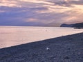 The sea and the pebbly shore are illuminated by the setting sun, the cloudy sky is colored by the sunset light Royalty Free Stock Photo