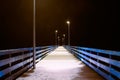 Sea pier covered with snow in night yellow lights from lampposts, mysterious path in darkness