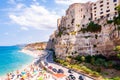 Sea promenade scenery in Tropea with high cliffs with built on top city buildings and apartments. Rotonda beach full of people.